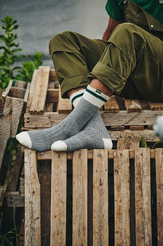 Personne portant des bas Growers & Co. assise sur des caisses en bois dans un jardin