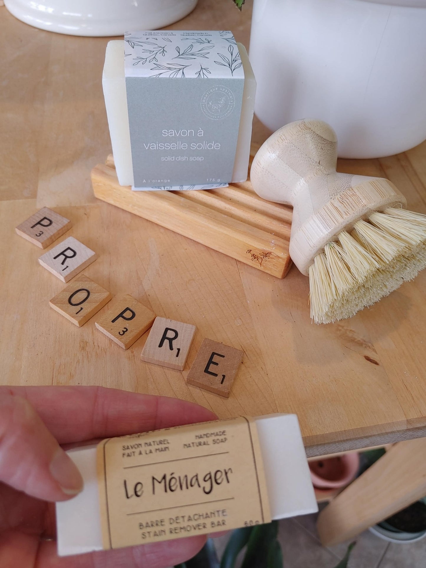 Ensemble de produits ménagers québécois comprenant brosse en bois, savon solide à l'orange et barre détachante vue de près.