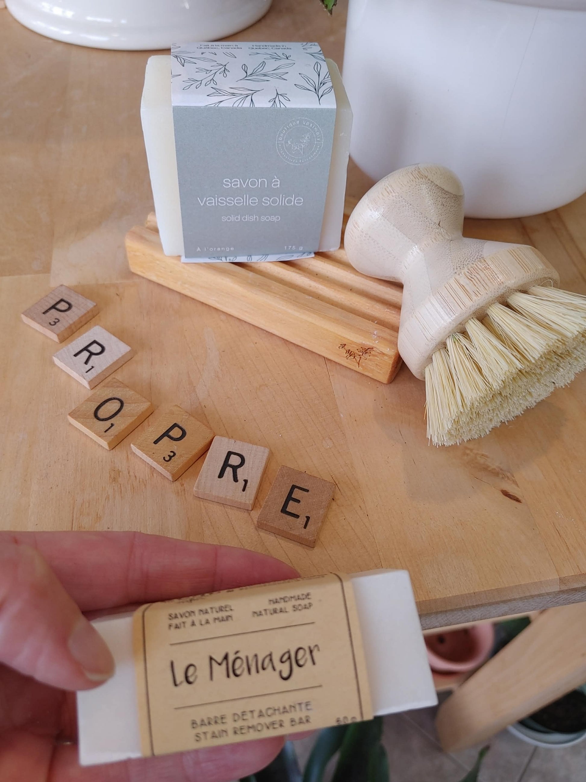 Ensemble de produits ménagers québécois comprenant brosse en bois, savon solide à l'orange et barre détachante vue de près.