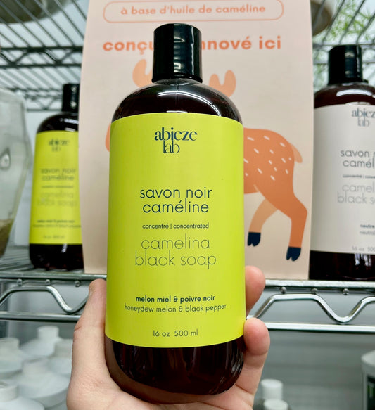 Main tenant une bouteille de savon noir a la cameline Abieze parfum melon miel et poivre noir