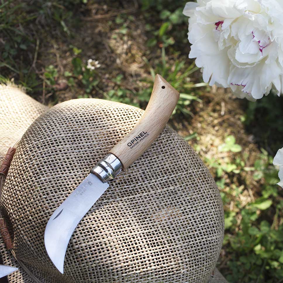 Couteau serpette Opinel ouvert déposé à côté de fleurs dans un décor de jardin