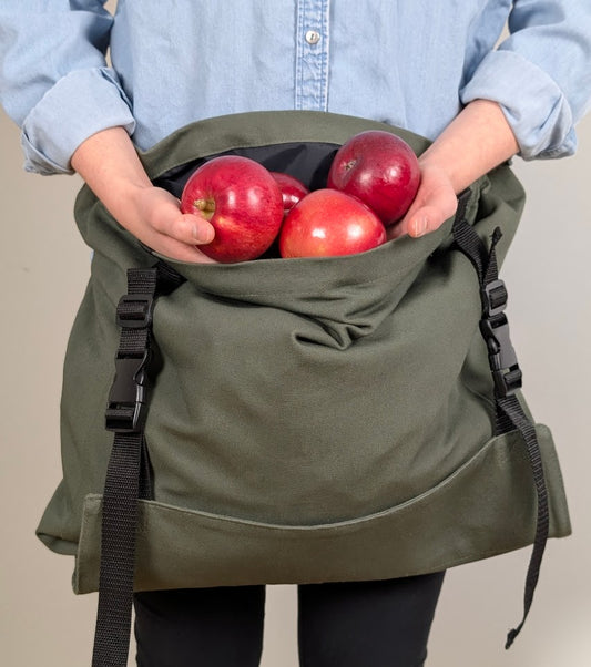 Sac de récolte porté en tablier et rempli de pommes, idéal pour les cueillettes au verger.