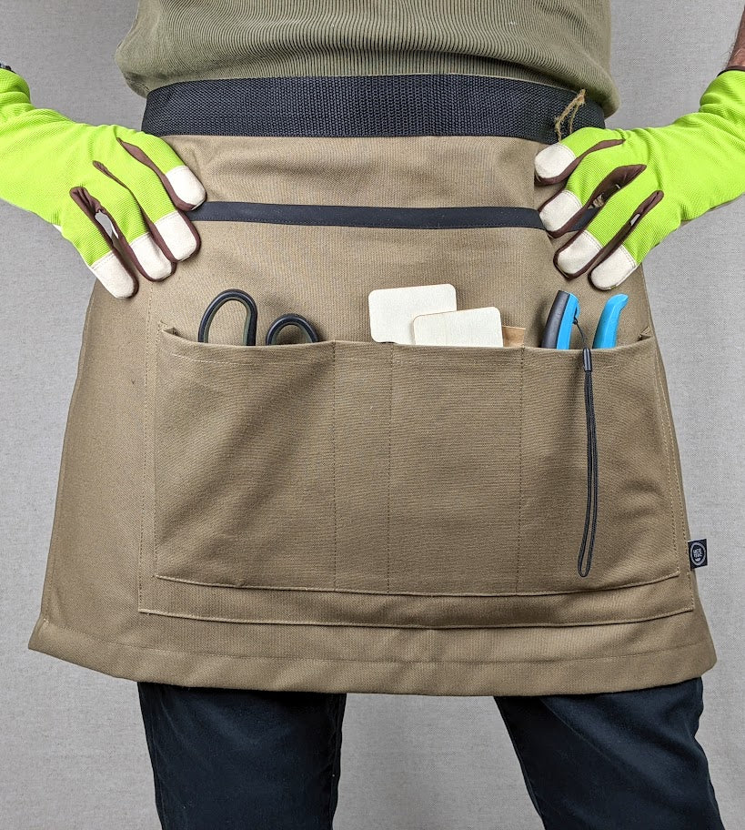 Personne portant le tablier ceinture de jardinage couleur taupe avec ses 4 poches remplies de petits outils.