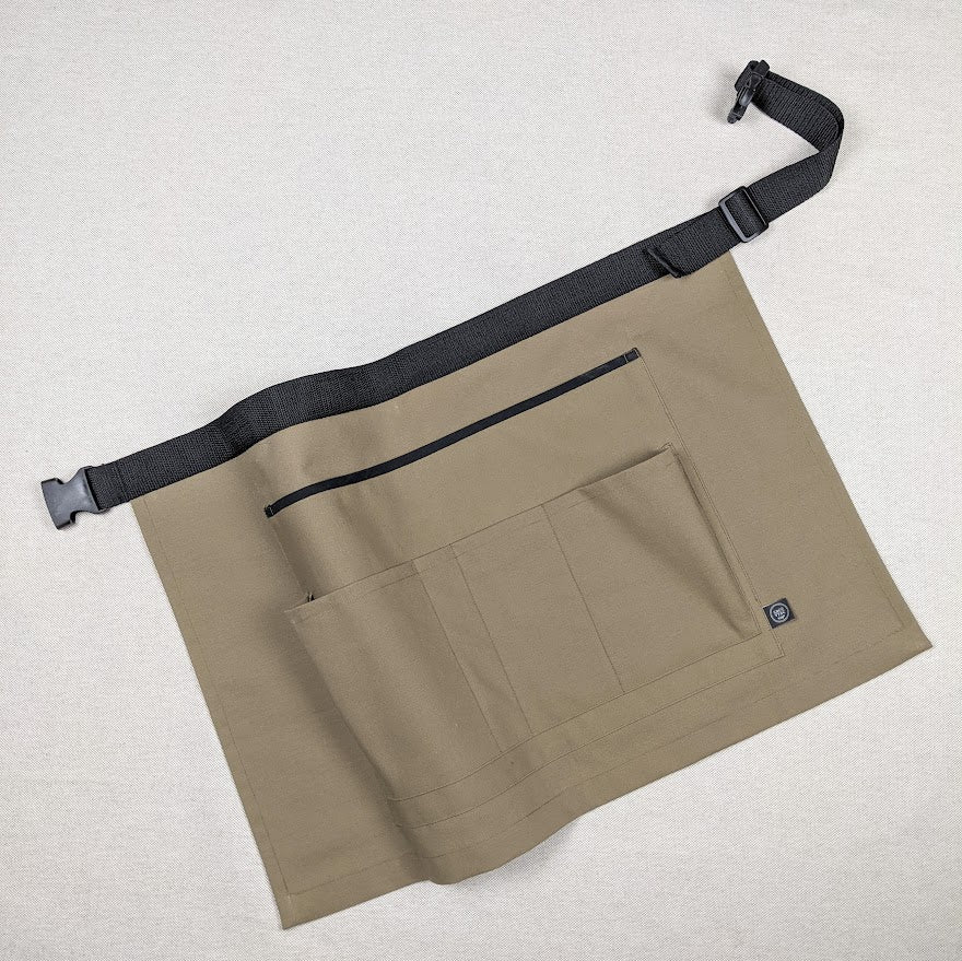 Tablier ceinture court de couleur taupe, présenté à plat pour montrer ses 4 poches de rangement.
